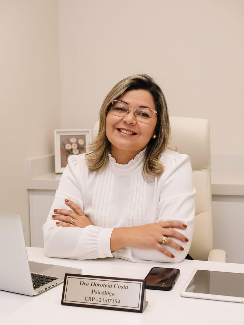 Doroteia Costa sentada à mesa do consultório, de braços cruzados, sorrindo